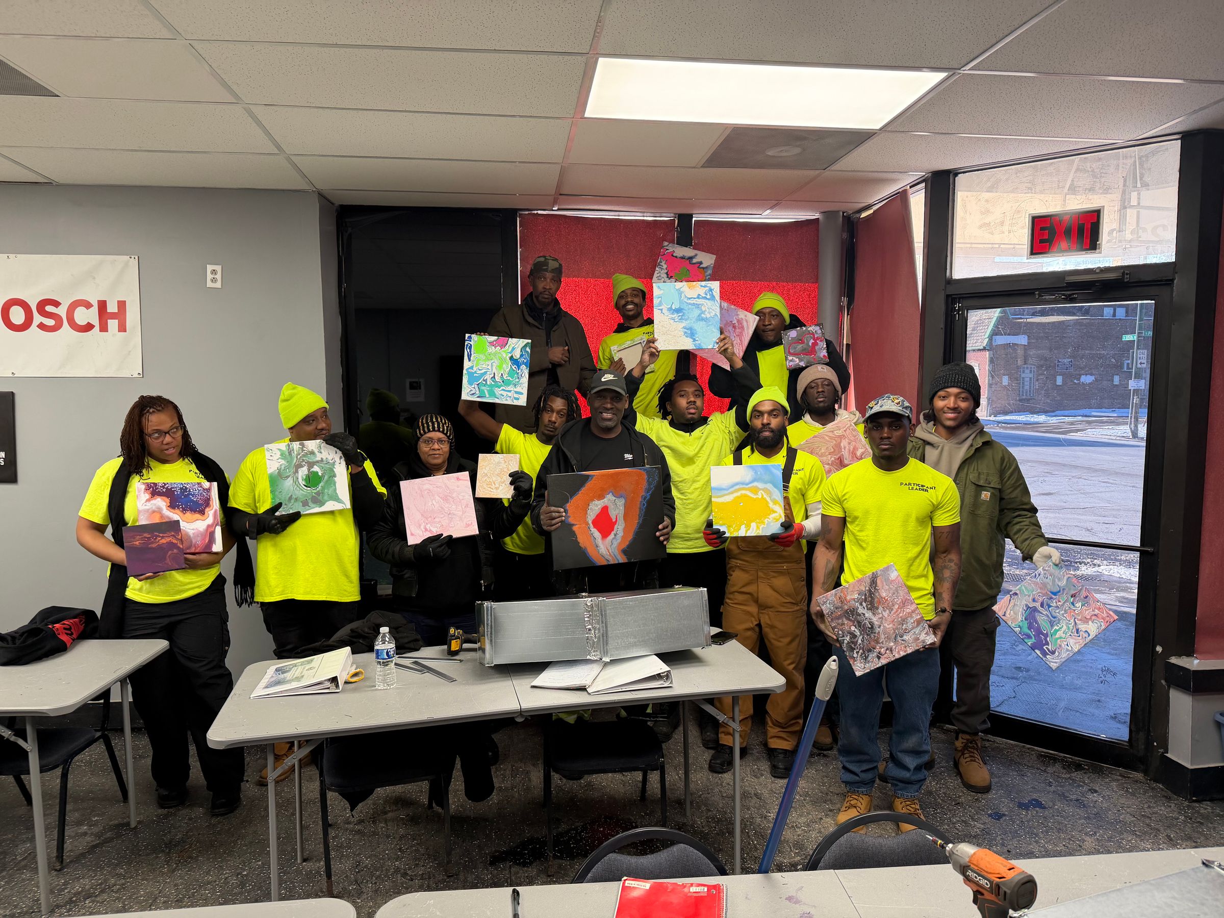 Bliss Global Corp. inaugural cohort holding their artwork — students in yellow shirts celebrating in the Roseland, Chicago training classroom